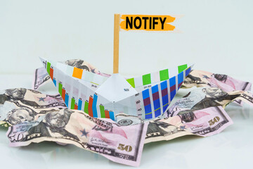 A paper boat from a business graph floats on a sea of money. The text is written on the flag -...