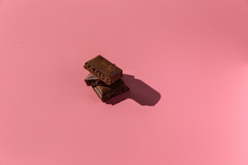 pieces of chocolate on a pink background with hard light
