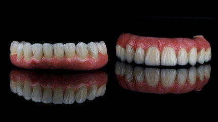 metal ceramic dentures with pink gums for the upper and lower jaw, filmed on black glass with reflection
