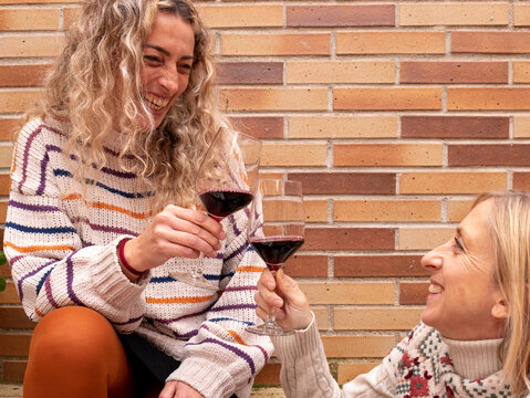 a low angle shot of two blonde females smiling and drinking wine together - cheers