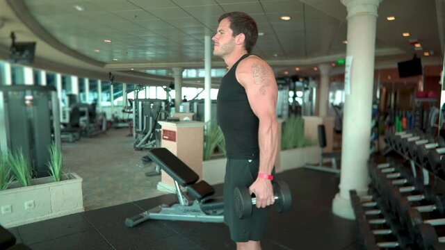 Strong young handsome man does dumbbell exercise in the gym