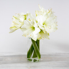 Bouquet of white lilies in a glass vase on a beige table against a gray wall