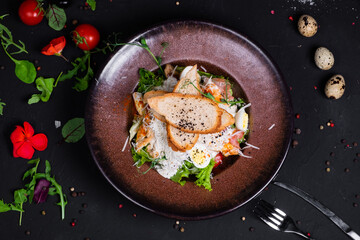Caesar salad with grilled chicken fillet and slices of bacon, with tomatoes and Caesar sauce. Sprinkled with Parmesan cheese with wheat croutons and quail egg. on a dark background