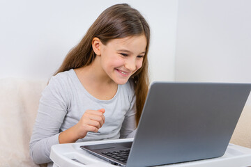 Portrait of attractive cute happy smiling girl 6-7 old sitting using laptop indoor white background distance learning