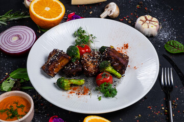 Grilled pork ribs in honey glaze with tomatoes and broccoli on a dark background