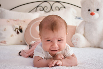 Newborn crying baby girl. New born child tired and hungry on white bed. Concept of crying unhappy baby.