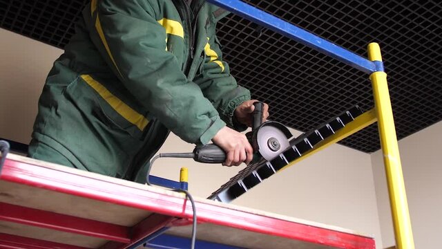 Worker cutting metal ceiling grid with angle grinder