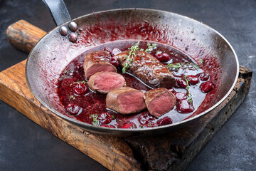 Traditional wild hare back filet braised with wild berries and cherry relish souse served as close-up in rustic frying pan on an old wooden board