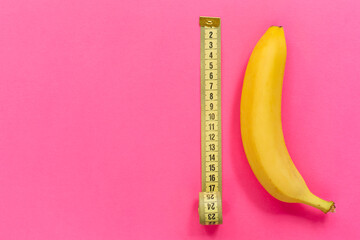 Yellow banana with measurement tape on pink background. Men penis size concept. Flat lay, top view,...