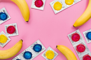 Composition with colorful condoms and bananas on pink background. Safe sex and contraceptive concept. Flat lay, top view, copy space.