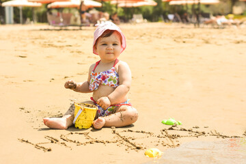 Cute adorable happy baby girl playing on the sandy beach near the sea. Family on resort. Summer holiday concept.