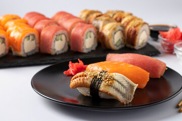 Asian food with sushi set of salmon, tuna and eel with philadelphia cheese on black plate on a white background. Served with soy sauce, wasabi and pickled ginger. Closeup