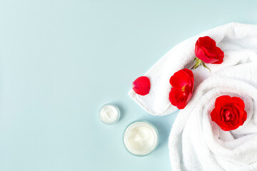 Spa and beauty. A white bath towel with red buds and two creams are on a blue background. Free space for text.