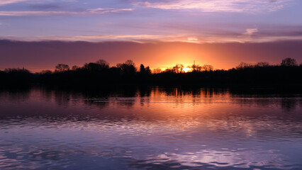 Amazing sunrise or sunset in rural scene. Symmetry of the sky in a lake. Clouds reflecting on the water. Quiet relaxing scene with a beautiful colorful cumulonimbus.