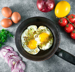 fried eggs in a pan with pepper and thyme on a gray background, fresh tomatoes,