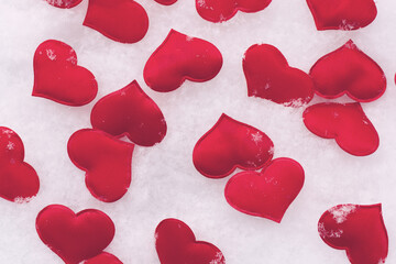 red hearts are scattered on the white snow. The background for creation. Horizontal photo. Snowflakes are winter.