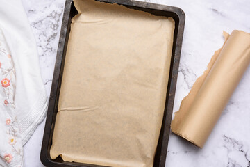 empty rectangular metal baking sheet and roll of brown parchment paper on white background