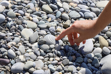 Finger presses on an unusual stone as if pressing button, close-up on pebble surface with copy space