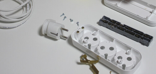 An extension cord for three inputs, which lies on a white table. Cord, sockets, white