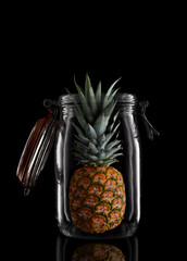 A whole Pineapple in a glass storage or canning jar isolated on black with reflection, with lid open.