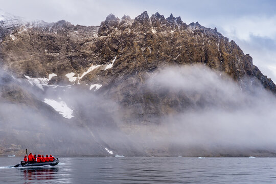 Surreal fog incircles a rocky snow covered island in Svalbard with zodiac in the foreground