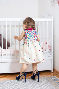 Adorable cute baby girl trying to wear her mother's high heels shoes. Funny little toddler child playing in her white scandinavian children room. Nursery with nordic stylish Happy mother's day concept