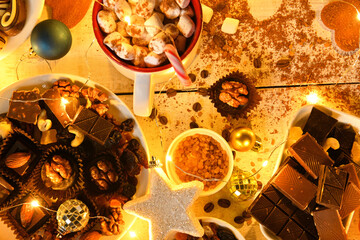sweet food top view background for merry christmas or new year holiday decoration with night illumination - chocolate candies, tangerines, cookies, marshmallow and cocoa latte on white wood