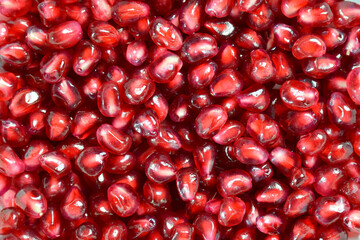 The whole background is covered with juicy bright red pomegranate fruit grains. Shot close-up