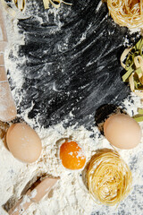 Freshly cooked pasta is lying on a dark surface dusted with flour. Italian pasta. Tagliatelle. Raw pasta. Italian pasta recipe. Top view, copy space