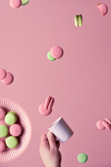 Levitation of macaroons, creative food concept. Flying macaroons, plate and hand with coffee cup. Trendy creative sweets background, monochrome image on pink paper.