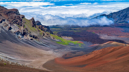 Haleakala Crater in Maui shows vibrant colors with blue sky and clouds in the distance.