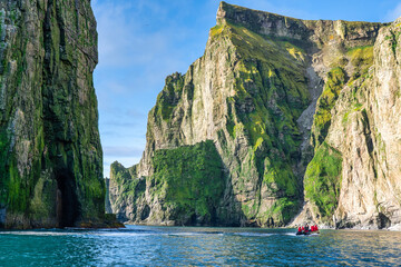 A zodiac cruises along side of picturesque massive rocky cliffs in Bear Island  Norway