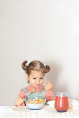 Adorable cute baby girl eating corn flakes for breakfast. Beautiful kid eat cereal with the milk in the kitchen. Healthy nutrition for small children. White background and copy space for text.