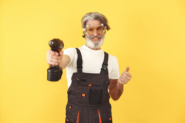 Worker in overalls. Man with tools stands against the background. Senior with screwdriwer.