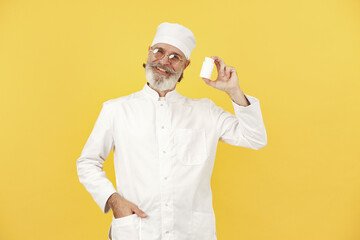 Smiling medical doctor with pills. Isolated over yellow background.