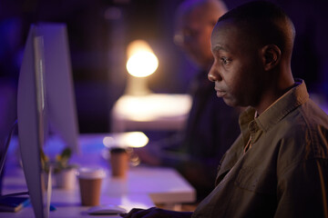 Side view shot portrait of serious young adult African American man using computer at work in evening, copy space