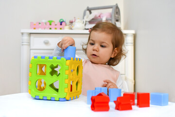 Cute adorable baby girl solves sorter puzzle. Toddler Having Fun with educational toys. Kid playing in nursery with nordic stylish. White scandinavian interior for children's room. 
