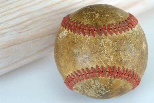 An Old And Well Used Baseball Is Shown Up Close, Next To A New, Wood Baseball Bat.