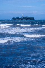 olar of the sea breaking and in the background a small island with a lighthouse