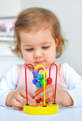 Cute adorable baby girl playing with colorful wooden bead roller coaster toy at home or kindergarten. Toddler child having fun with educational toys. Kid playing in nursery.