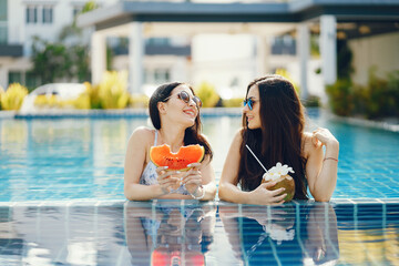 two girls tanning and having fruit by the pool