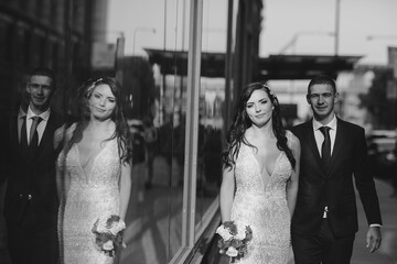 Naklejka premium Elegant wedding couple walking in a summer city. Man in a blue suit. Woman in a white elegant dress with bouquet of roses