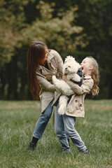Mother and her daughter playing with dog. Family in autumn park. Pet, domestic animal and lifestyle concept. Autumn time.