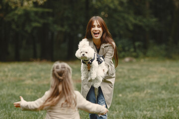 Mother and her daughter playing with dog. Family in autumn park. Pet, domestic animal and lifestyle concept. Autumn time.
