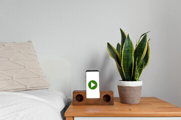 A closeup of a bedside table with a snake plant and a mobile phone with a green play button on the screen