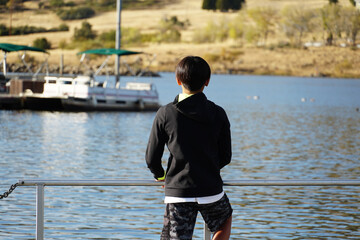 Fototapeta na wymiar Young sporty Asian boy looking at the view on a wood pier at the Lake. Teenager concept