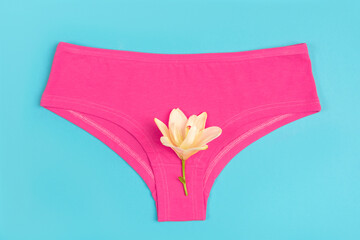 Pink underpants and flower on blue background, close up. Concept Keep your vagina healthy and...