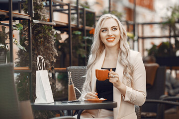 Lady drinks a coffee. Woman sitting at the table. Blonde in a white suit.