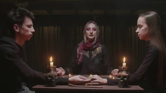 Young couple visits young witch female fortune teller. They holds each ather hands and closes eyes