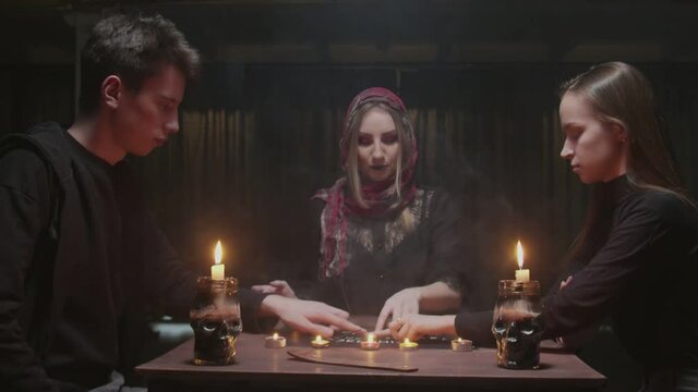 Witch female fortune teller tries to speak with ghost. Two women and one man uses Ouija Board Spirit Game